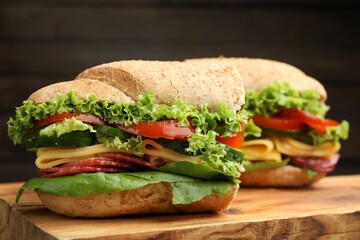 Pieces of tasty baguette sandwich with smoked sausage, cheese and vegetables on wooden board...