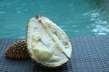 Fresh ripe durian on wicker table near swimming pool outdoors, closeup. Space for text