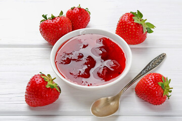 Tasty strawberry jam in bowl and fresh berries on white wooden table, closeup
