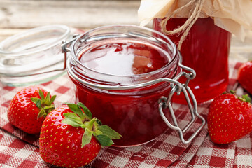 Tasty strawberry jam in glass jars and fresh berries on table, closeup