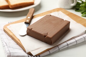Block of tasty chocolate butter and knife on light table, closeup