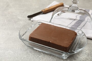 Block of tasty chocolate butter in glass keeper on grey textured table, closeup