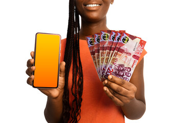 Beautiful Black woman lady smiling holding 200 Ghanaian cedi notes and showing pointing phone with blank screen to the camera over white background. Hand holding Ghanaian currency notes