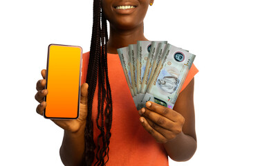 Beautiful Black woman lady smiling holding United Arab Emirates dirham notes and showing pointing phone with blank screen to the camera over white background. Hand holding UAE currency notes