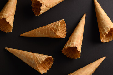 A variety of waffle cones are scattered on a dark surface, showcasing their crispy texture and...