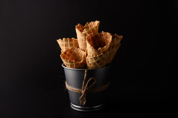 Several waffle cones are stacked in a rustic bucket, prepared for filling with various ice cream...