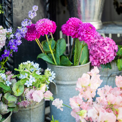 A colorful display of various flowers as a hydrangea in vases and buckets at an outdoor flower shop.