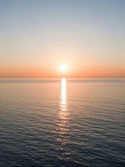 Naklejka premium Open ocean during golden hour, soft gradient sky from peach to blue, sun near the center casting long reflection, no land in sight, peaceful and minimal