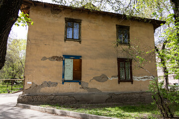 Old two-story house with peeling plaster and boarded window surrounded by spring trees