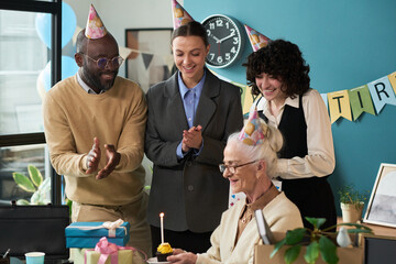 Senior Caucasian woman sitting at table holding cupcake with lit candle while celebrating retirement