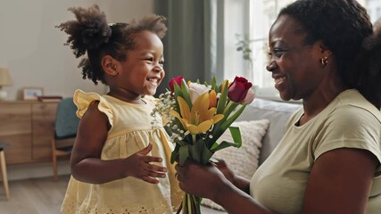  small   African American  daughter presenting  bouquet of flowers   to  mom in modern living room