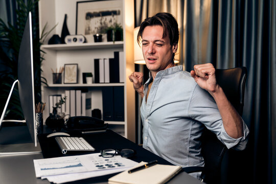 Sales manager working on desk with stretching arm up and down manner at night time at modern home office with monthly sales report for quarter presentation summary of profitable product. Pecuniary.