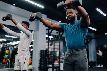 Two black men lifting weights during functional training in gym