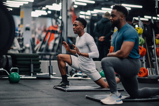 Two male athletes stretching legs on mats in gym