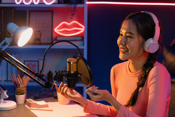 Smiling creative young beautiful Asian influencer talking in channel with positive podcast speech...