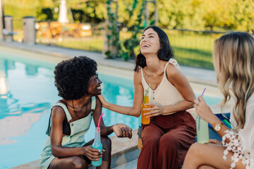 Young women laughing and drinking by the poolside during summer vacation