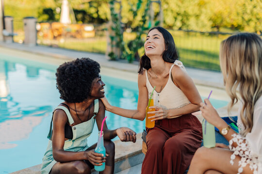 Young women laughing and drinking by the poolside during summer vacation - Powered by Adobe