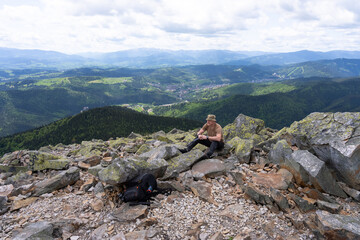 A man sits on a rock with a knife in his hand.