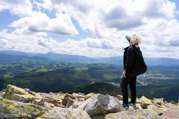 A woman drinks water on top of a mountain.