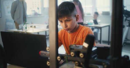Talented Young Boy Sitting at Table, Writing Code for Advanced Automated 3D Printer on Laptop Computer. Primary School Student Learning Programming in Modern Classroom. Interactive STEM Education.