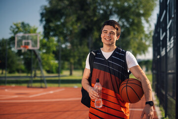 Smiling basketball player holding ball and water bottle on court