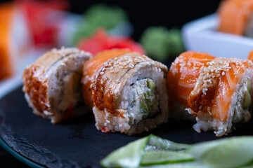 A black plate contains a variety of sushi rolls.
