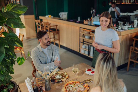 Waitress serving pizza to customers in pizzeria restaurant