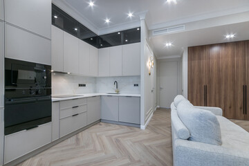 The interior of the studio apartment with a modern design. Built-in wardrobe made of 
dark wood. White kitchen set.