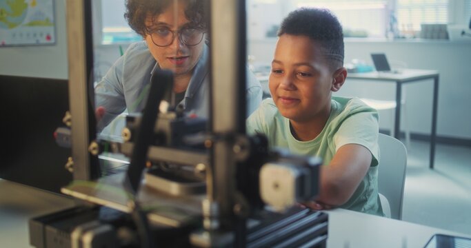 African American Elementary School Student Watching Printing Process on Automated 3D Printer on Programming Lesson. Teacher Educating Smart Young Boy in Modern Classroom. Interactive STEM Education.
