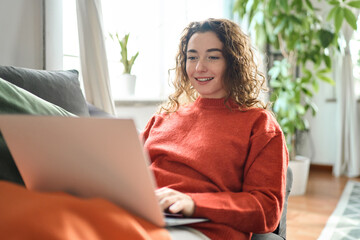 Young lady looking at computer ordering sale products on website, watching videos or elearning. Relaxed happy woman sitting on couch using laptop at home surfing, doing online ecommerce shopping,