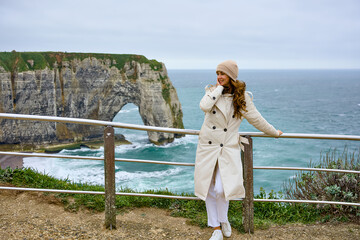 Stylish woman in coat smiling at Etretat cliff viewpoint