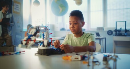 Obraz premium Elementary School Student Studying Robotic Arm Model During Science and Technology Lesson in Modern Classroom. Young African American Boy Dreaming to Become Engineer. Interactive STEM Education.