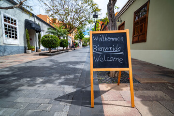 Tafel mit dem Wort Willkommen in deutsch, spanisch und englisch auf einer Einkaufsstraße in Los...