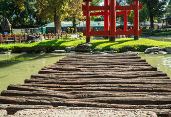 A wooden bridge over a pond with a red gate