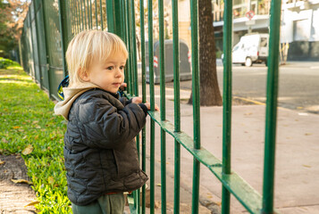 A young child is standing in front of a green fence
