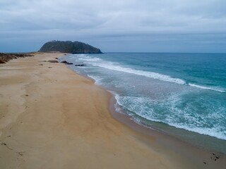 Aerial view of Point Sur State Historic Park in Big Sur, California, USA. The lighthouse sits atop a volcanic rock formation, waves crash on the sandy beach.