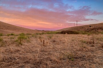 Dry grassy field in San Juan Bautista, California, USA, at sunset. The sky is pink and blue, and...