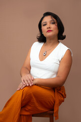 Elegant businesswoman sitting on a stool, with serious facial expression. Ideal decision making, female empowerment, career choices, personal growth. Vertical studio portrait with beige background.