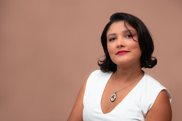 Beautiful brown skin woman smiling discretely, looking at camera. Perfect for female empowerment, beauty, self-love and feminine themes. Ample copy space on beige background.