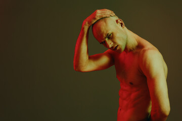 Strong man posing with a thoughtful expression, illuminated by dramatic red light against a dark...