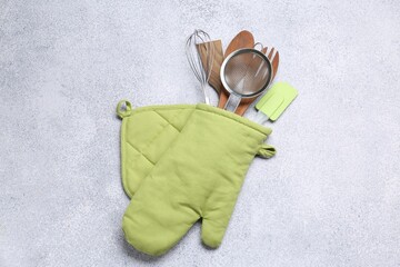 Different kitchen utensils in oven mitten on light table, top view