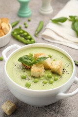 Tasty pea cream soup with croutons and basil served on grey table, closeup