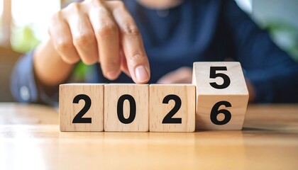 Naklejka premium Hand flipping wooden blocks displaying the year 2026 on a table, indicating the upcoming year
