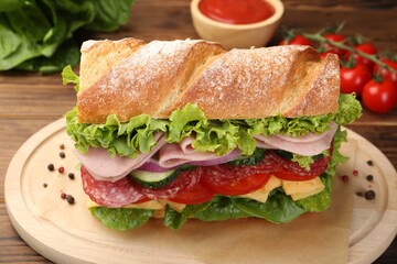 Tasty baguette sandwich with ham and vegetables on wooden table, closeup