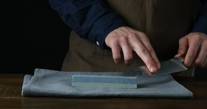 Man sharpening knife with sharpener at wooden table against black background, closeup