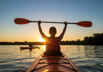 Two people are enjoying recreational kayaking on a lake or river during a beautiful sunset, with one person holding their paddle triumphantly.