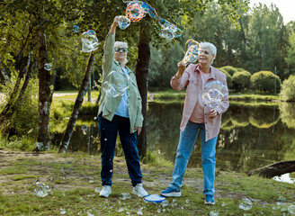 Lifestyle and people concept. Two elderly sisters blowing soap bubbles in a summer park.