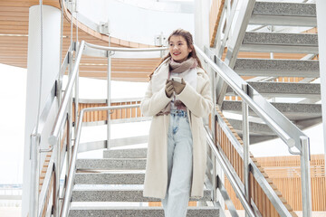 Woman in winter clothes talking on phone in the city. Woman stay near modern stairs.