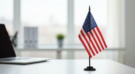 Small US desk flag on an office desk with a blurred laptop and window in the background