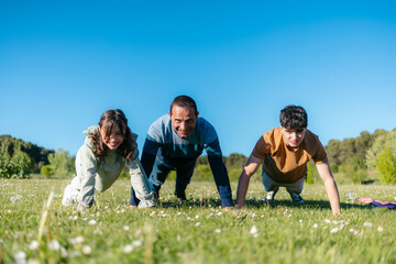 Father, daughter and son are doing push ups in a meadow during a family picnic